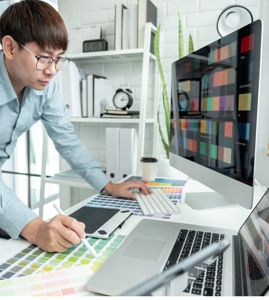 Male graphic designer is standing to choosing color swatch samples on multiple screens and working graphic design with technology while sketching on tablet digital in modern office